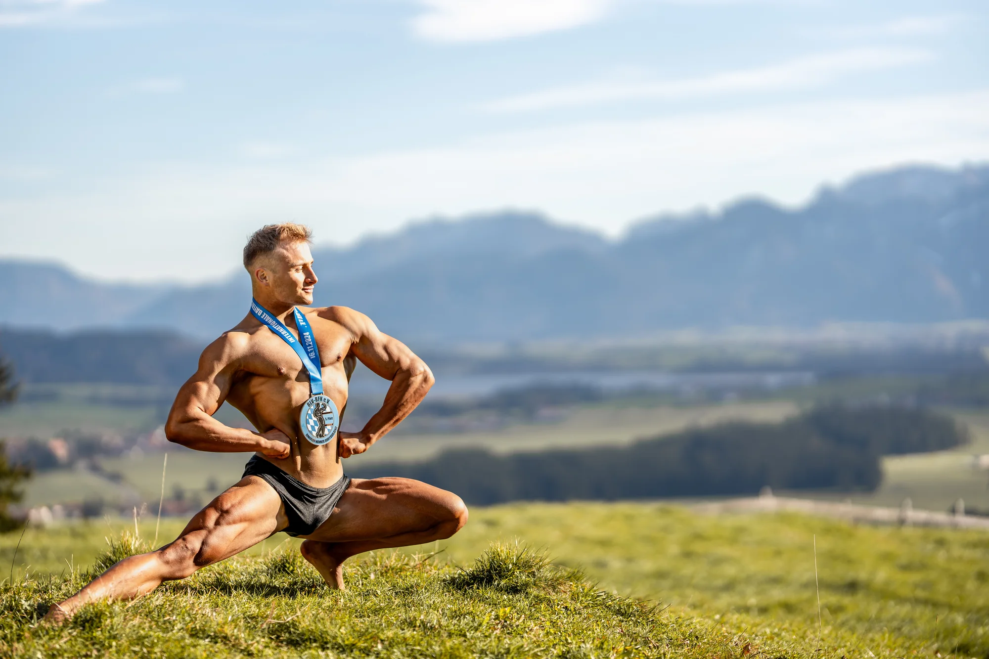 Toni posiert mit Medaille auf einer Bergwiese, im Hintergrund Allgäuer Berge.