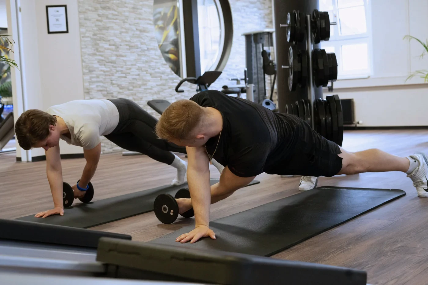 Athletiktraining: zwei Sportler bei einer Stützübung mit Kurzhanteln auf der Matte.